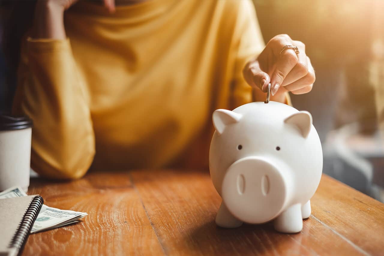Woman placing coin in Piggy Bank - There are pros and cons to the 401(k) savings plan.